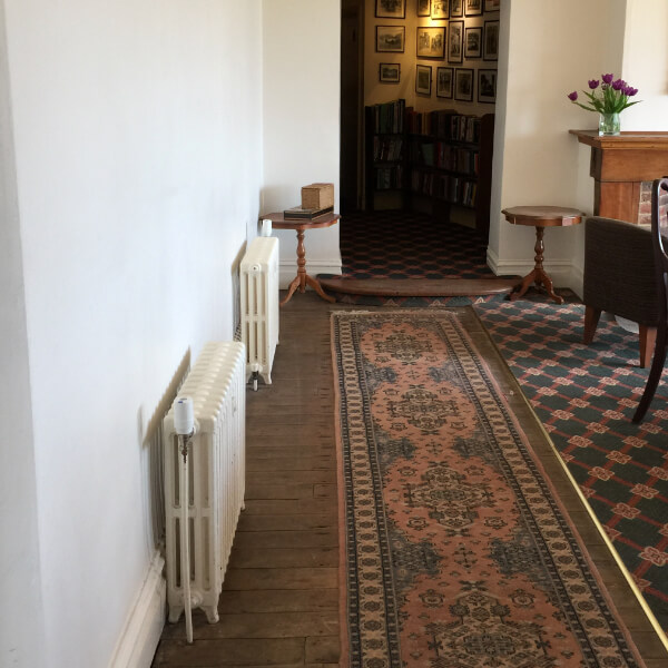 A photo in Bossington Hall Hotel, showing a white wall with 2 cast iron radiators in front of it. There are Wireless Radiator Valves mounted at the top of each radiator.