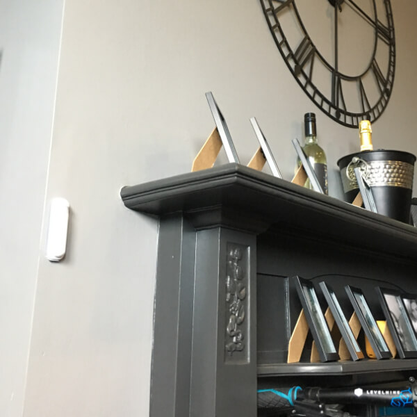 Photo of a fireplace with photo frames on the top and a large clock above it on the wall. There is a Wireless Room Sensor to the left of the fireplace.